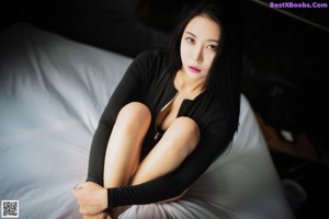 A woman in a black bodysuit sitting on a bed.