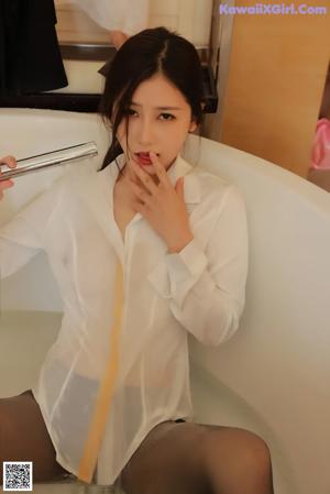 A woman in a white shirt and black skirt sitting in a bathtub.