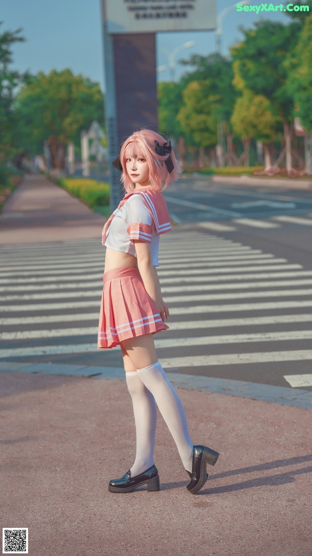 A woman in a pink and white outfit is walking across the street.