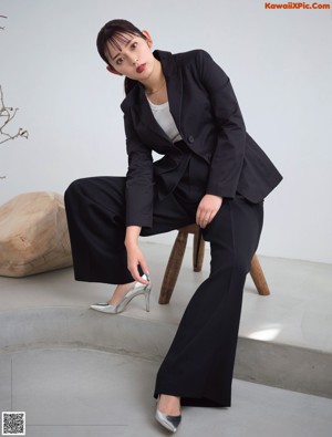 A woman in a white shirt and blue skirt sitting on a pink wall.