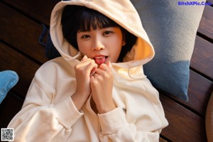 A naked woman in a white hoodie sitting on a bed.