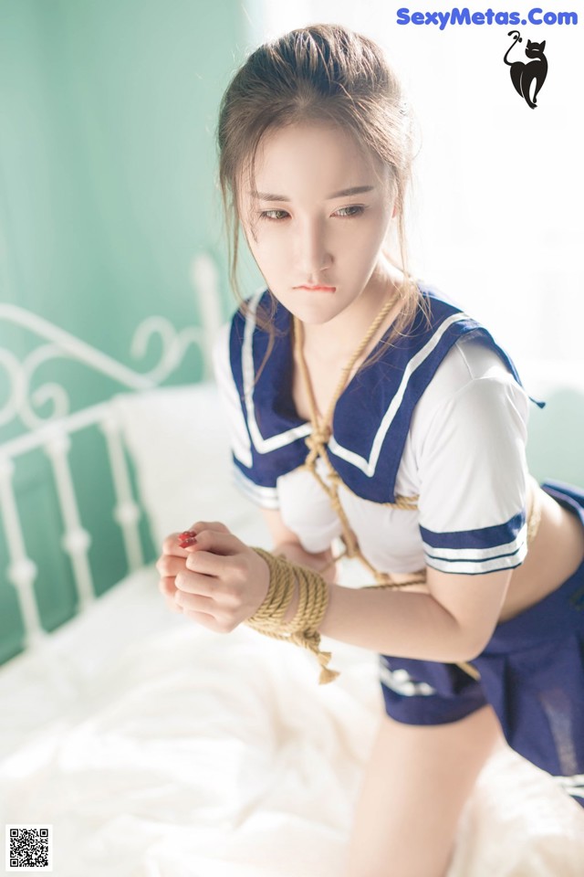 A woman in a sailor outfit is tied up on a bed.