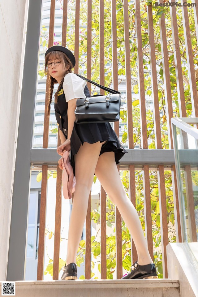 A woman in a black skirt and hat is walking up some stairs.