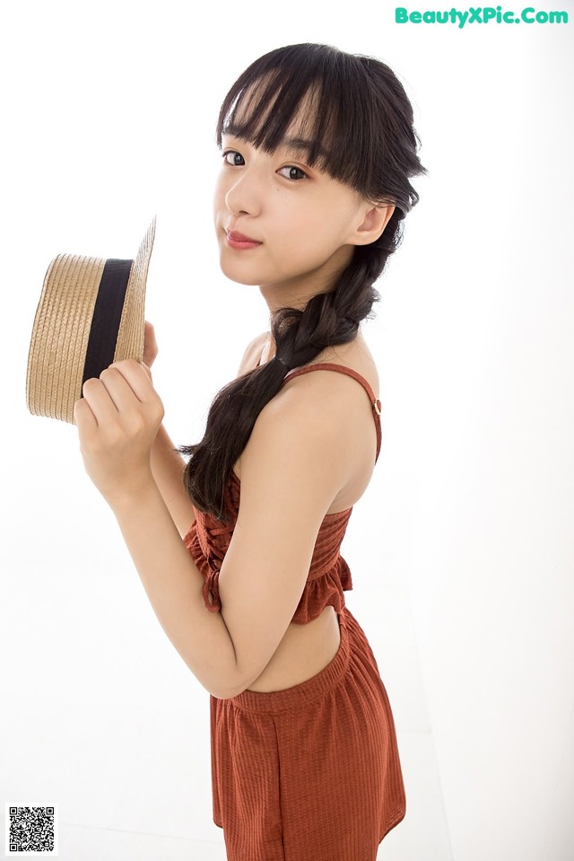 A young woman holding a straw hat in her hand.