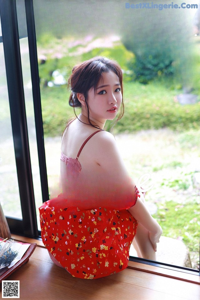 A woman in a red dress sitting on a window sill.