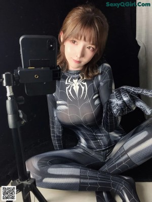 A woman in a black and silver spider suit holding a cell phone.