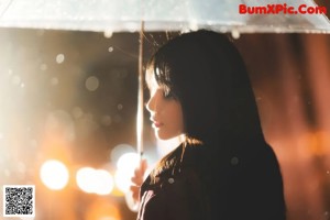 A woman crouching down in the rain holding an umbrella.